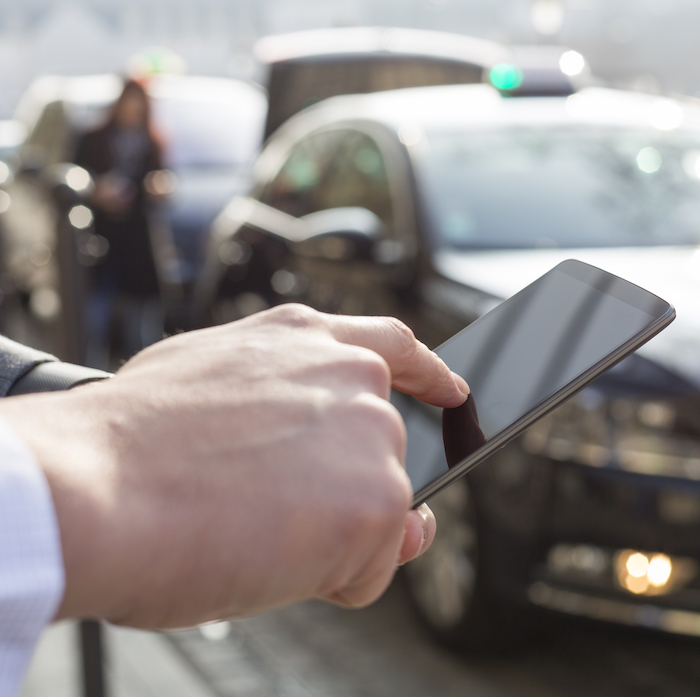 A man's hand holds a smartphone to select an option while a taxi cab waits in the background